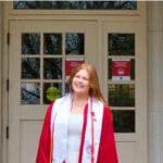 Smiling woman in graduation gown in front of a door