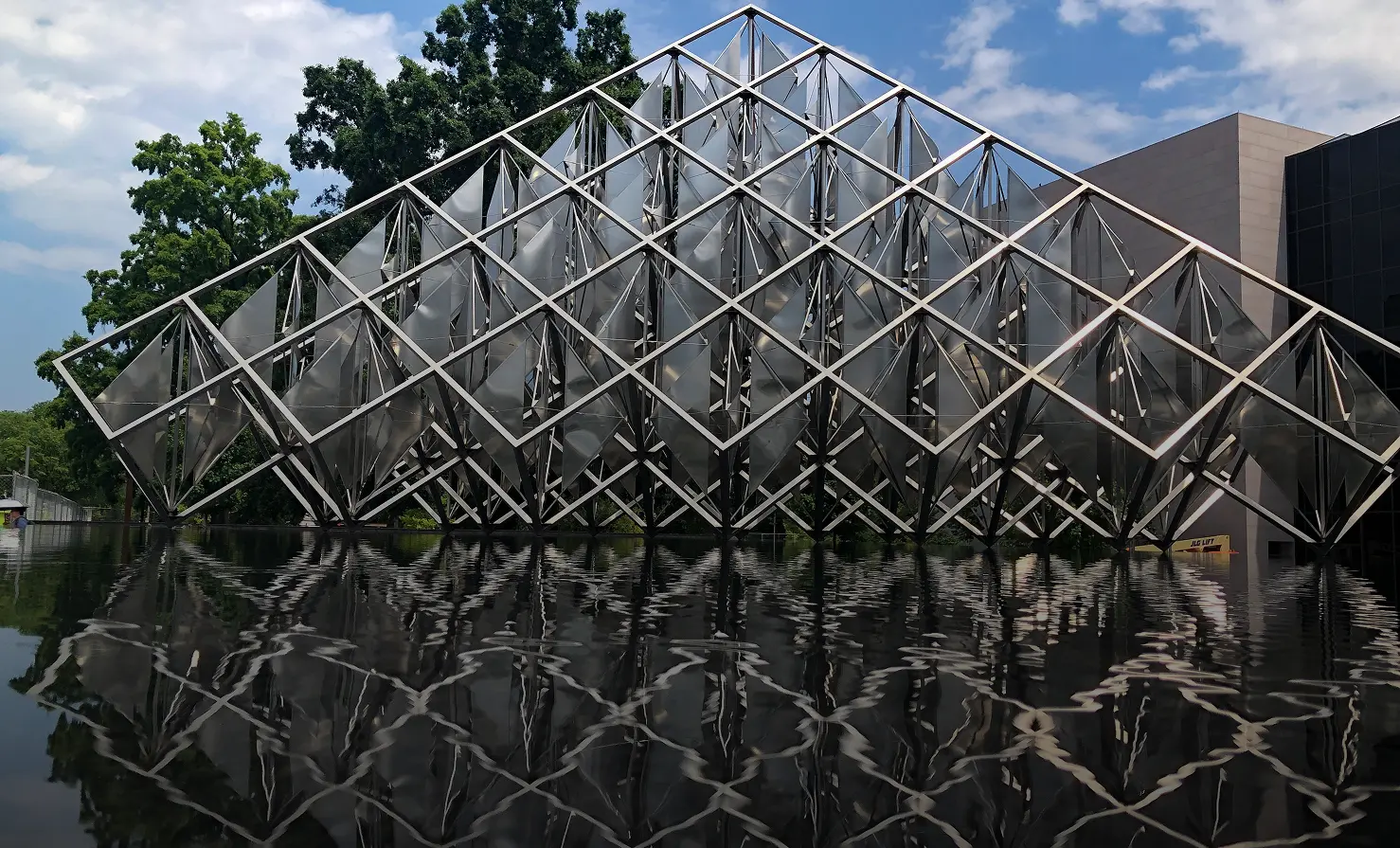 A large metal building reflects in calm water, creating a striking visual contrast.