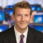 Man sitting in suit in front of screens posing for camera